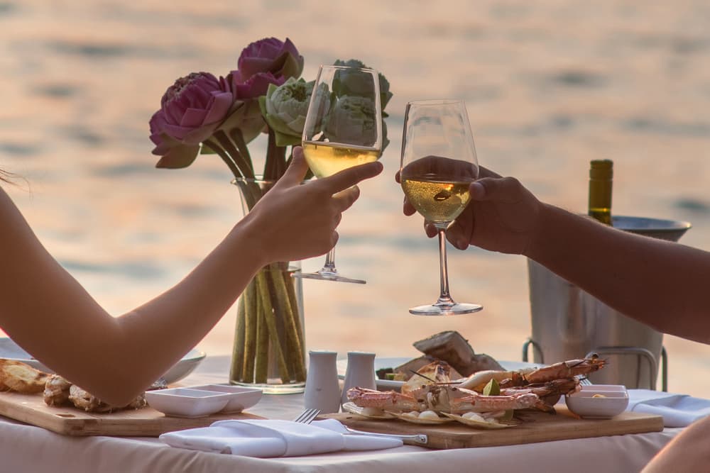 Couple toasting wine glasses during a romantic dinner in Phuket with sunset views